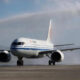 White commercial airliner with a blue stripe on a runway; water spray trails behind as it lands on a wet tarmac.