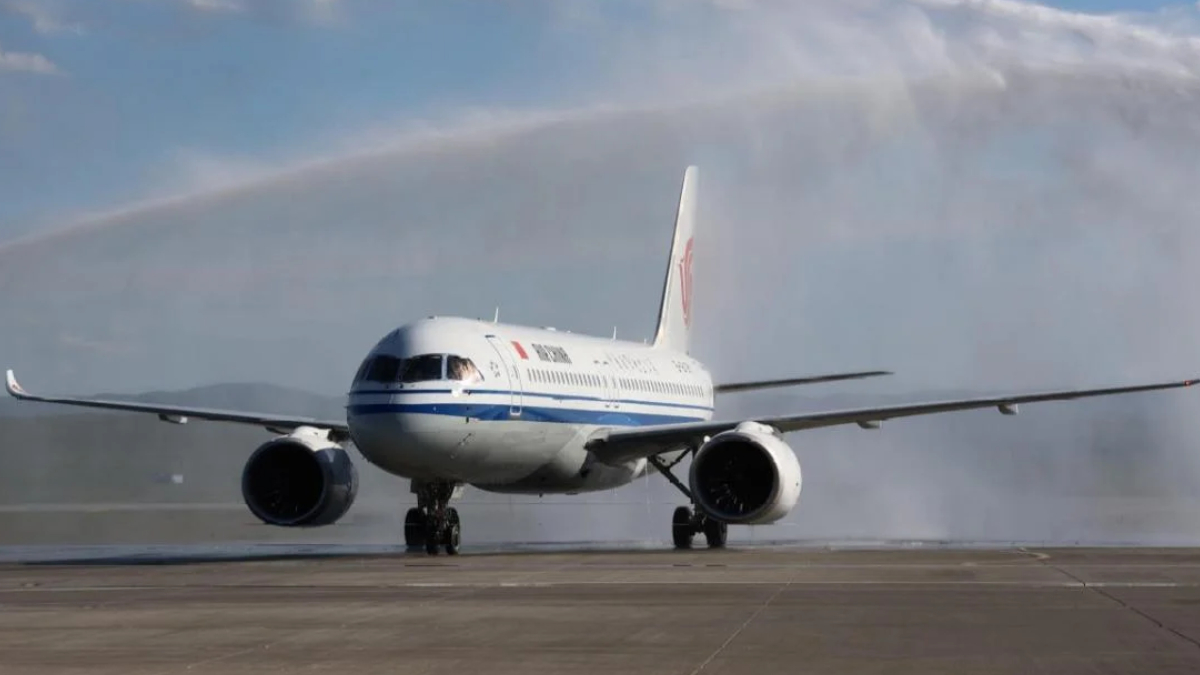 White commercial airliner with a blue stripe on a runway; water spray trails behind as it lands on a wet tarmac.