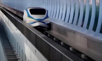 High-speed train gliding along an elevated curved track beside a glass-walled tunnel.