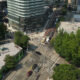 Aerial view of a busy urban intersection with cars, buses, and tall modern buildings surrounded by trees.