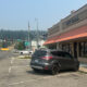 City street view in front of a beige City Hall with red awning; a gray SUV is parked in a diagonal handicap space by the storefronts in the foreground.