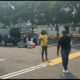 People set up gear in a parking lot beside a black SUV with open doors; a woman in yellow speaks to a man approaching.