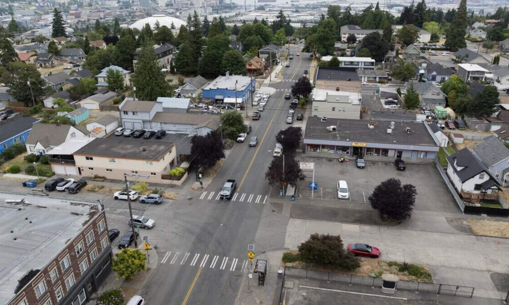 Aerial view of a small town intersection with crosswalks, storefronts, and parked cars in a grid of streets.