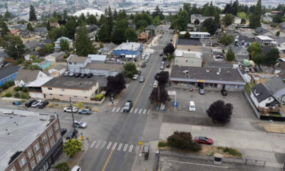 Aerial view of a small town intersection with crosswalks, storefronts, and parked cars in a grid of streets.