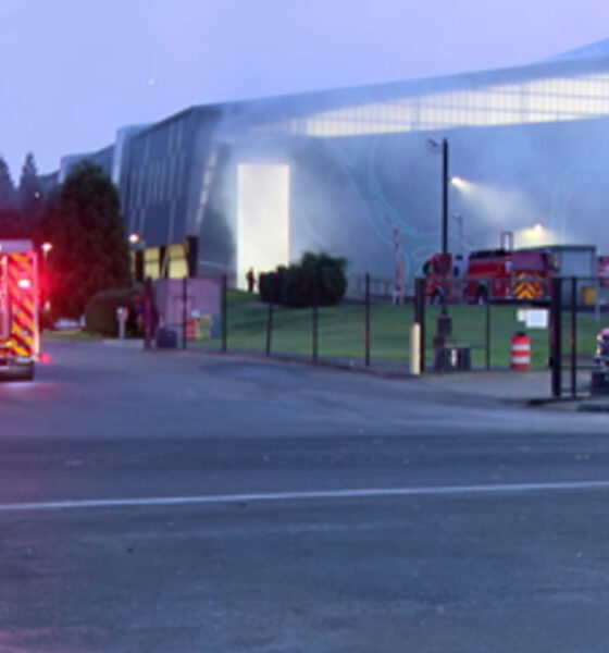 Fire trucks with flashing lights parked outside a large modern building at dusk, responding to an incident.