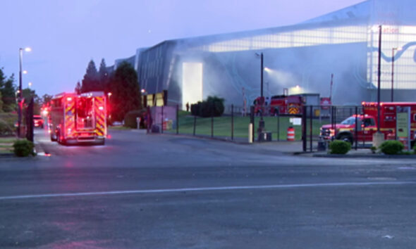 Fire trucks with flashing lights parked outside a large modern building at dusk, responding to an incident.