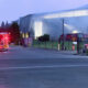Fire trucks with flashing lights parked outside a large modern building at dusk, responding to an incident.
