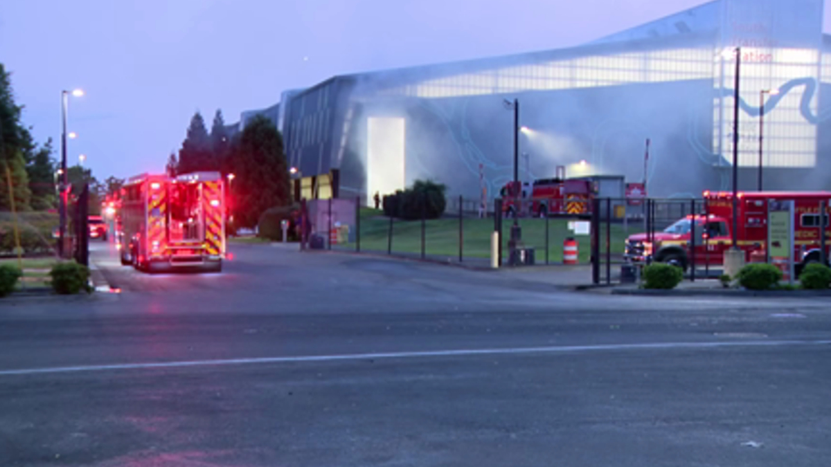 Fire trucks with flashing lights parked outside a large modern building at dusk, responding to an incident.