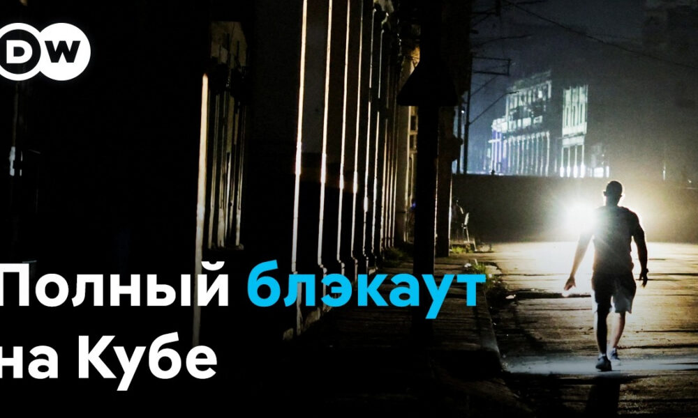 DW logo in the top-left; a man walks alone on a dark street at night with a bright backlight, caption reads 'Полный блэкаут на Кубе'
