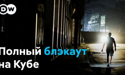 DW logo in the top-left; a man walks alone on a dark street at night with a bright backlight, caption reads 'Полный блэкаут на Кубе'