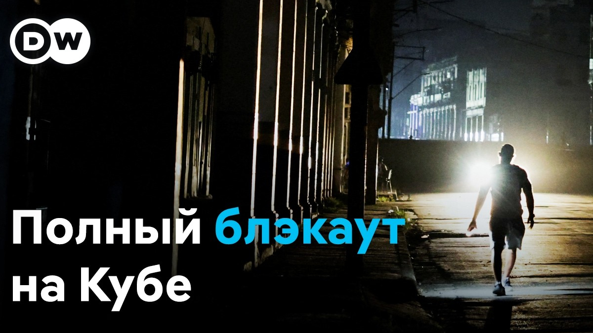 DW logo in the top-left; a man walks alone on a dark street at night with a bright backlight, caption reads 'Полный блэкаут на Кубе'