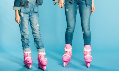 Two people wearing ripped jeans in pink inline skates stand on a bright blue backdrop, holding hands.