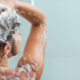 Person washing their hair in the shower, with white shampoo foam on the head and shoulders (back view)