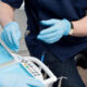 Dentist in blue scrubs and gloves handling dental drill over a patient chair with tray and controls nearby.