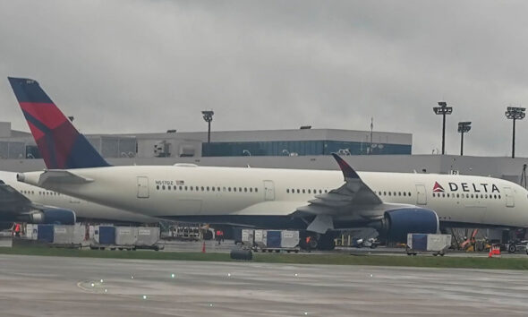 Delta airplane parked at a gate with a jet bridge attached and ground support equipment nearby.