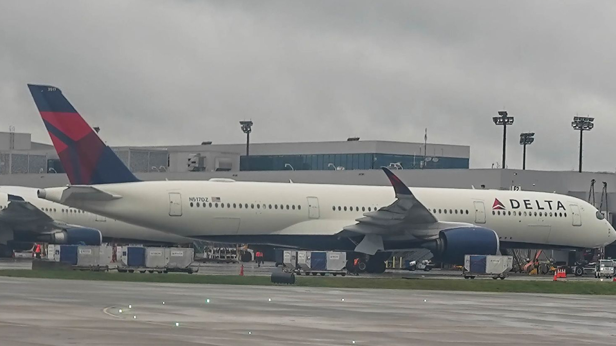 Delta airplane parked at a gate with a jet bridge attached and ground support equipment nearby.