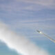 Two rockets angled upward, leaving white exhaust trails across a blue sky.