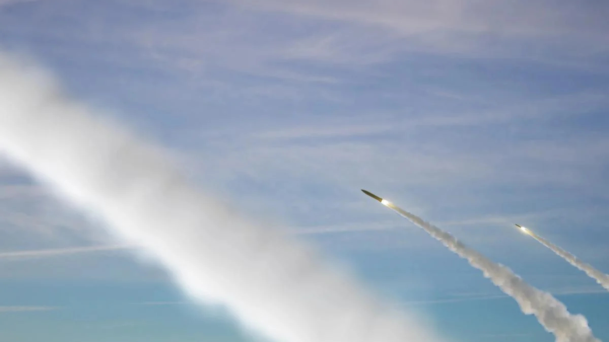 Two rockets angled upward, leaving white exhaust trails across a blue sky.
