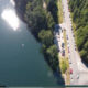 Aerial view of a blue lake with a tree-lined shore beside a busy road and line of parked cars on the edge of a forested area.