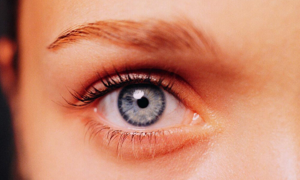Close-up of a blue eye with long eyelashes and subtle makeup, looking straight ahead.