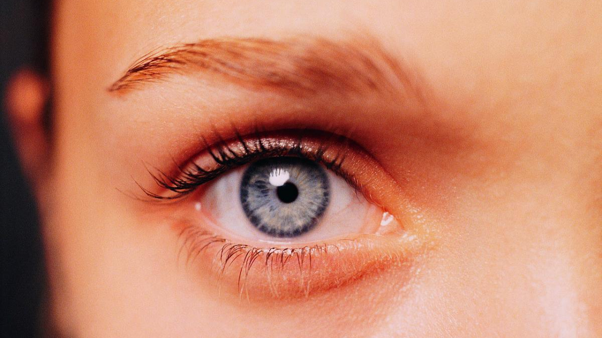 Close-up of a blue eye with long eyelashes and subtle makeup, looking straight ahead.