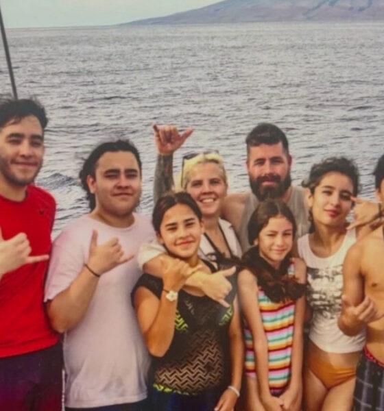 Group of smiling people of various ages posing together on a boat by the sea, with water and distant shore in the background (Woods Family).