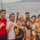 Group of smiling people of various ages posing together on a boat by the sea, with water and distant shore in the background (Woods Family).