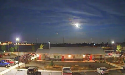 Nighttime view of a single-story building with a parking lot and cars, under a cloudy sky with a bright moon.