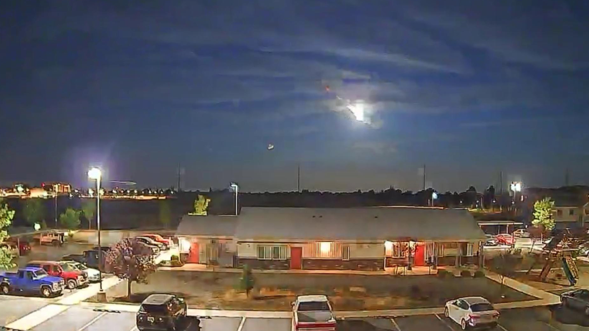 Nighttime view of a single-story building with a parking lot and cars, under a cloudy sky with a bright moon.