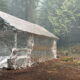Aluminum-foil wrapped shelter in a forest clearing, with hoses running around and a sprinkler spraying mist nearby.