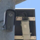 Outdoor surveillance camera mounted on a metal pole beside an electrical box and wiring.