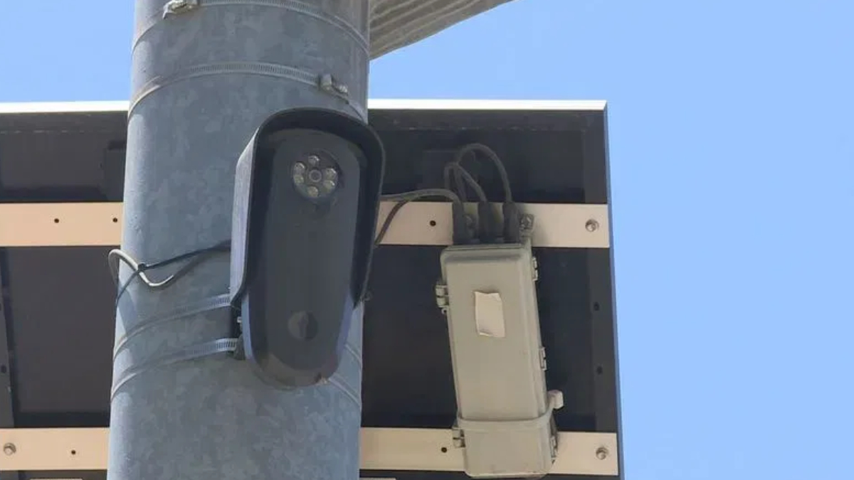 Outdoor surveillance camera mounted on a metal pole beside an electrical box and wiring.