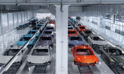 Bright automotive factory with rows of partially assembled cars on an assembly line in a bright, white-washed facility.
