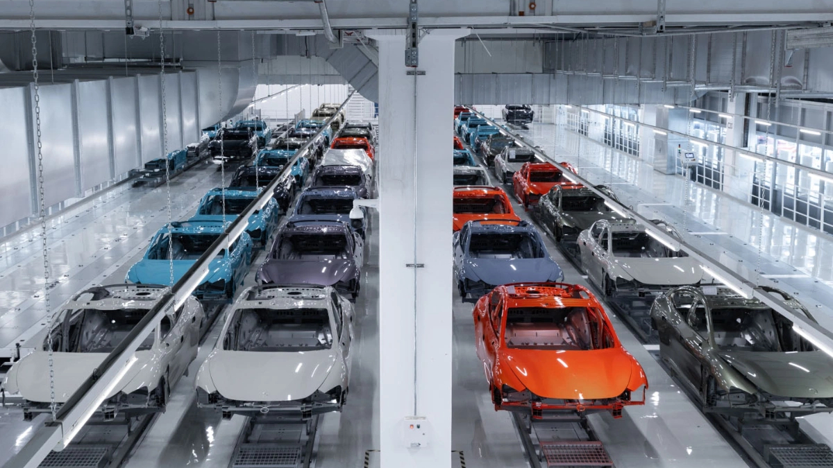 Bright automotive factory with rows of partially assembled cars on an assembly line in a bright, white-washed facility.