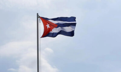 Cuban flag waving on a tall flagpole against a pale blue sky.