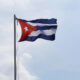 Cuban flag waving on a tall flagpole against a pale blue sky.