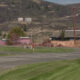 Rural scene featuring a pink wall and buildings, utility poles, and a grassy foreground with hills in the background beyond the road.