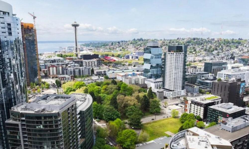 Aerial view of downtown Seattle with the Space Needle in the center, surrounded by glass skyscrapers and a green park in the foreground.