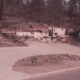 Residential street with collapsed, debris-filled foundations and damaged walls from a recent disaster; scattered rubble along the road edge.
