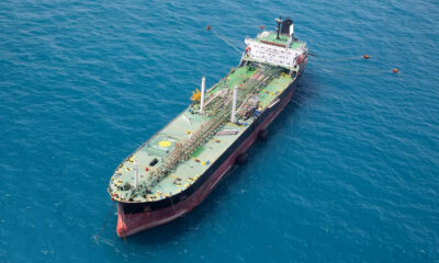Aerial view of a large oil tanker with a green deck and red hull floating in deep blue open water.