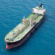 Aerial view of a large oil tanker with a green deck and red hull floating in deep blue open water.