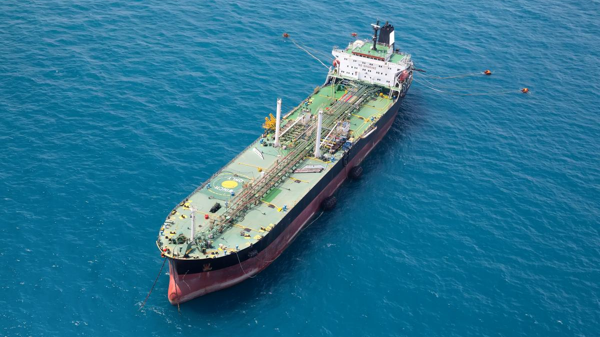 Aerial view of a large oil tanker with a green deck and red hull floating in deep blue open water.