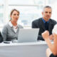 Panel of three professionals in business attire interviewing a candidate; a laptop and notes on the table.