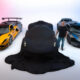 A black car is draped in a cover between a yellow and a blue sports car in a bright studio.