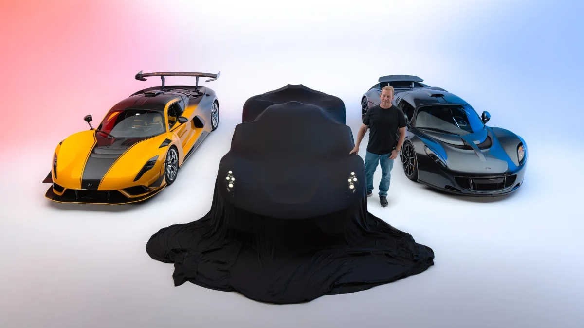 A black car is draped in a cover between a yellow and a blue sports car in a bright studio.