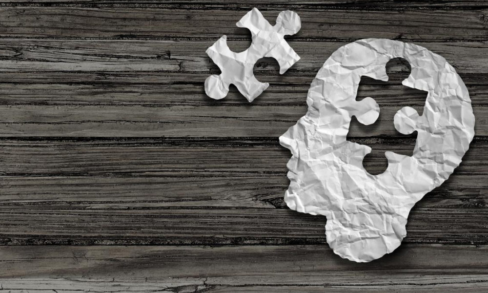 Crumpled white paper shaped like a human head with puzzle pieces on a dark wooden background