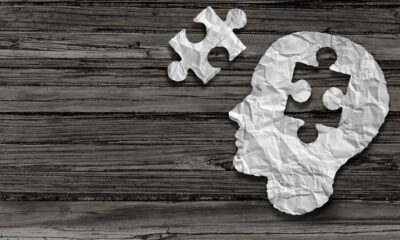 Crumpled white paper shaped like a human head with puzzle pieces on a dark wooden background