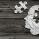 Crumpled white paper shaped like a human head with puzzle pieces on a dark wooden background
