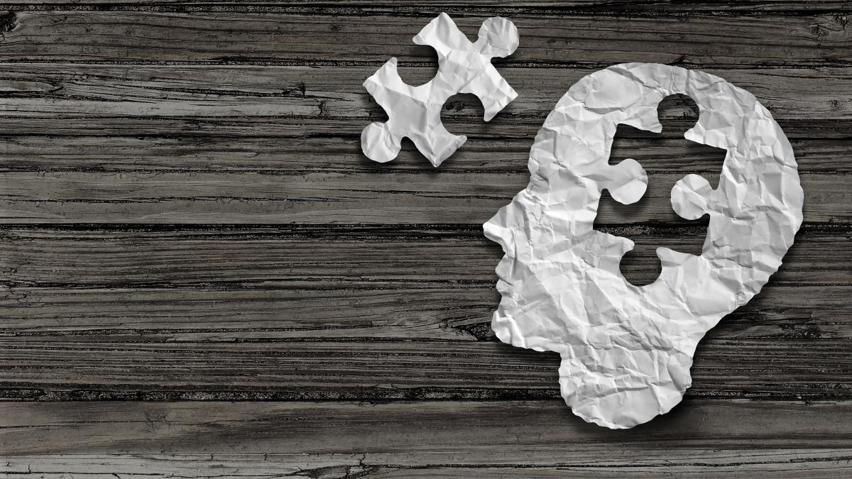 Crumpled white paper shaped like a human head with puzzle pieces on a dark wooden background