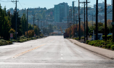 Wide empty street in a city neighborhood, power poles line both sides with trees and distant buildings on the skyline.